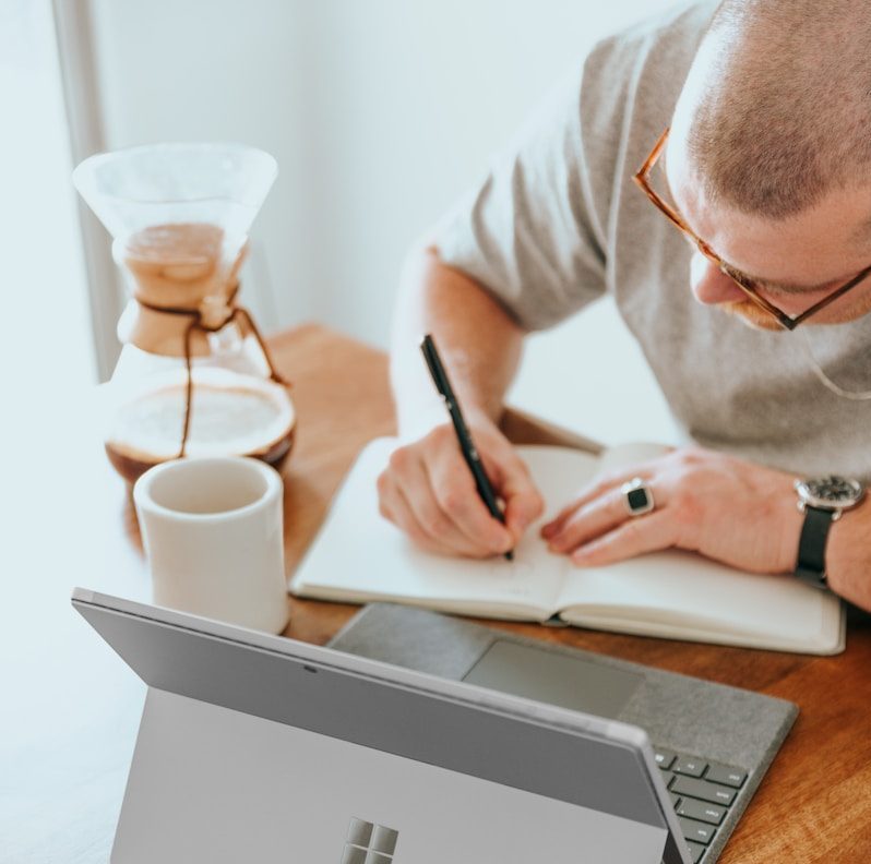 a man sitting at a table writing on a notebook