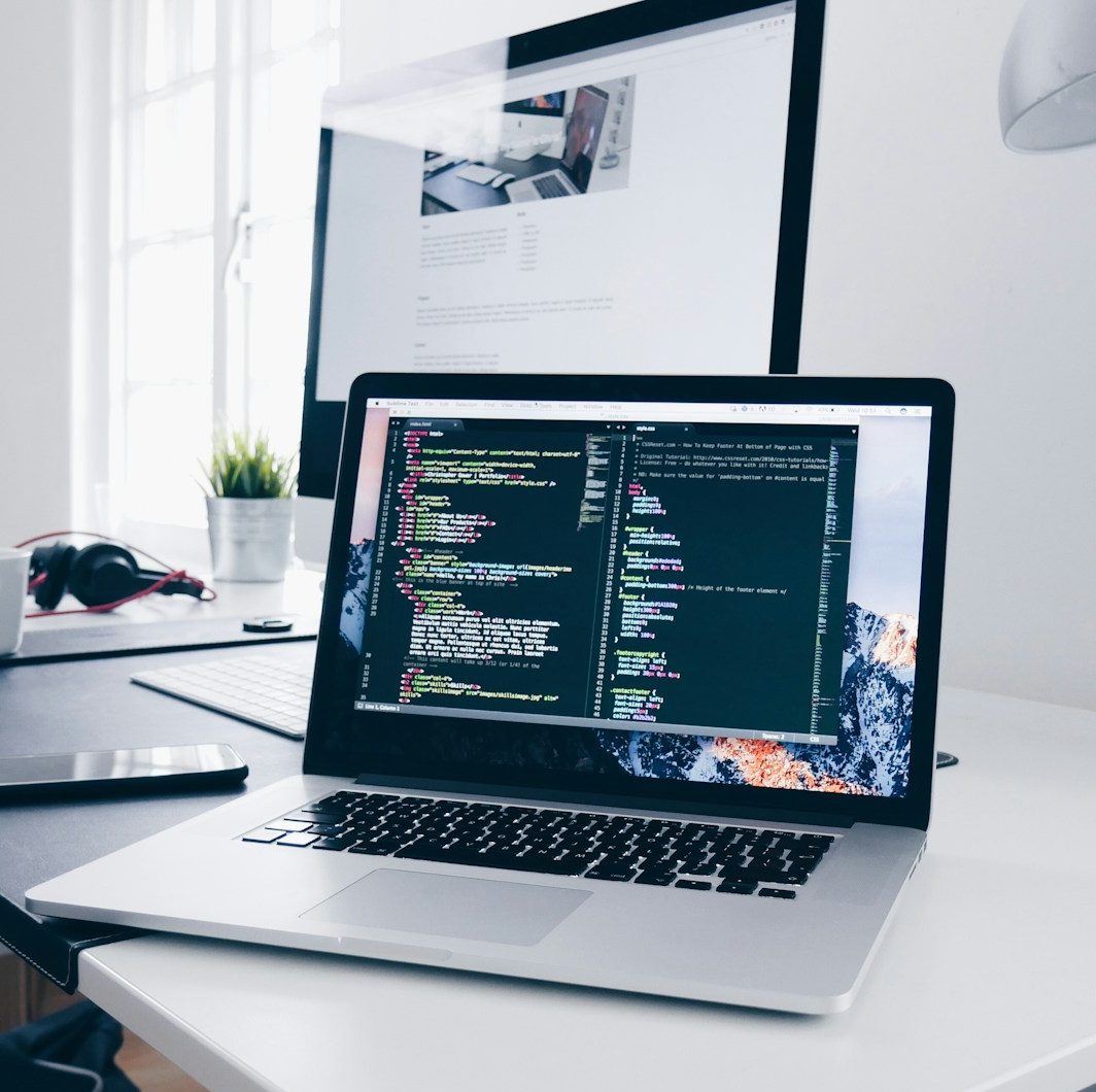 A MacBook with lines of code on its screen on a busy desk